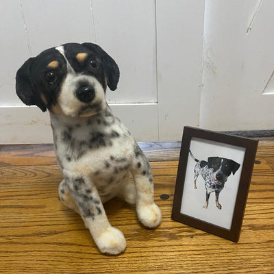 Stuffed animal replica of a brown and white dog beside a framed drawing of him