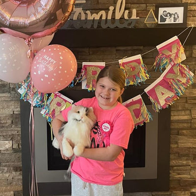 Girl at her birthday holding the stuffed animal that looks like her white dog